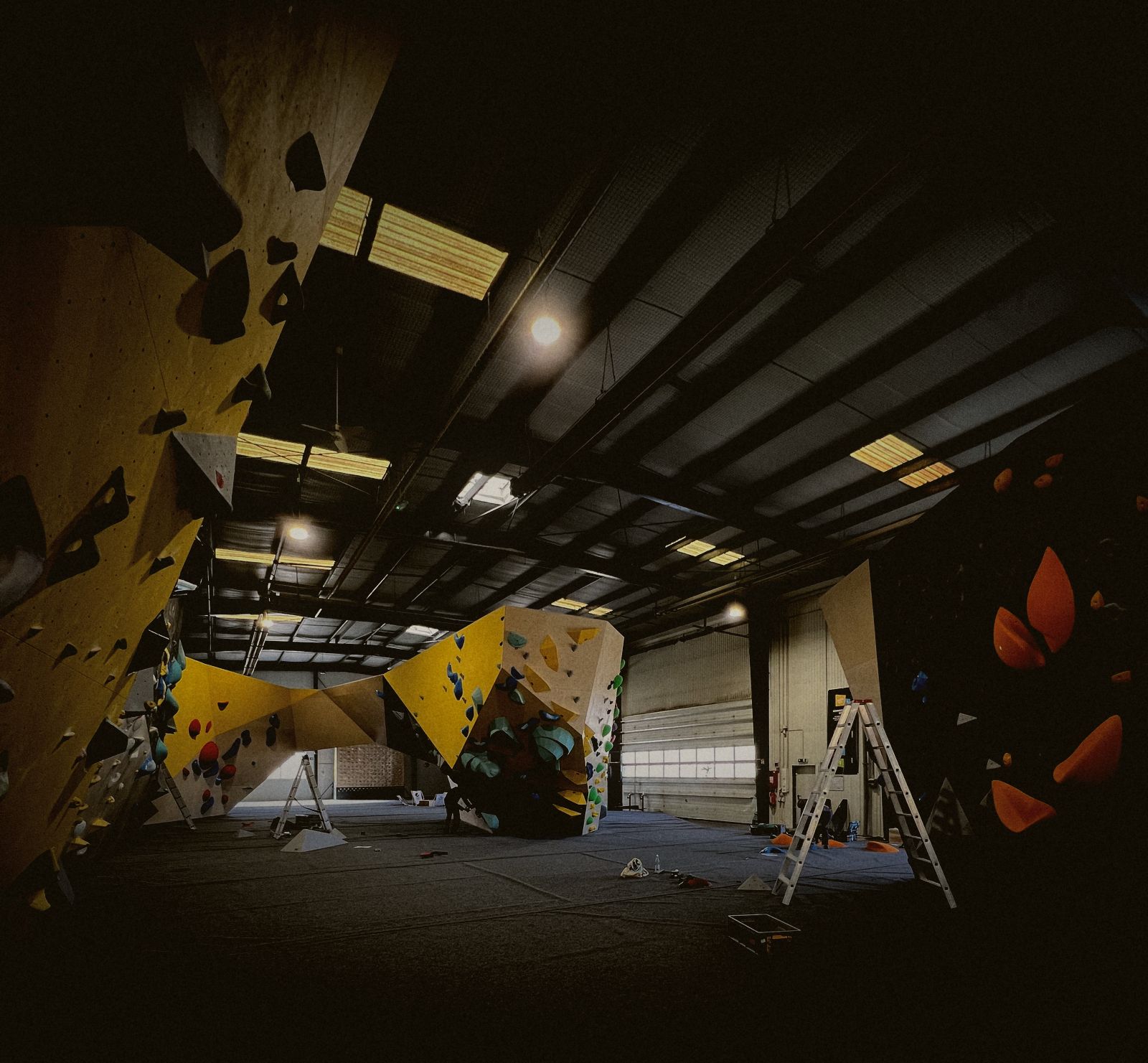 Blick durch eine Boulderhalle mit gelben Wänden und Leitern während des Schraubens