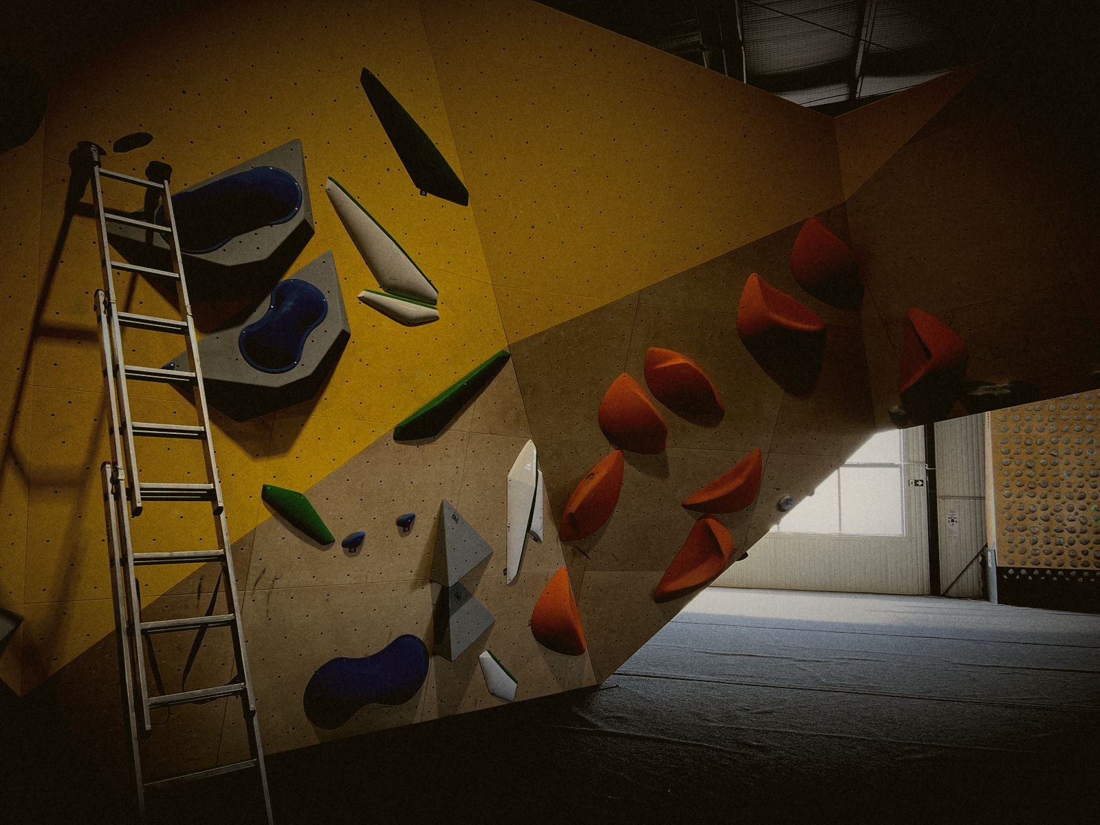 Orange und blaue Griffe auf gelben und hellen Holzplatten, links eine Leiter
